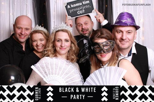 Hostia na svadobnej oslave sa zabávajú vo fotobúdke s rekvizitami ako korunky, vejáre a vtipné tabuľky počas Black & White party.