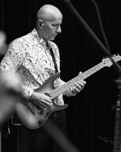 Čiernobiely detailný záber na gitaristu zo skupiny KOLOREZ band hrajúceho na elektrickú gitaru počas vystúpenia.