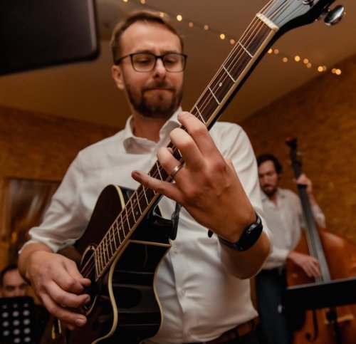Gitarista z kapely KOLOREZ band hrá na akustickú gitaru počas svadobného vystúpenia, v pozadí je vidieť kontrabasistu.