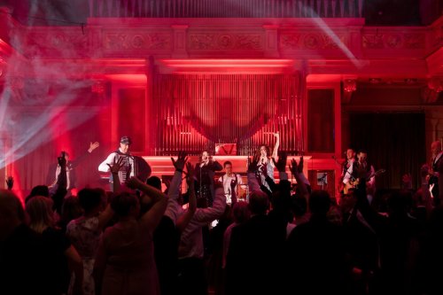 Hudobná skupina KOLOREZ band vystupuje na pódiu pred nadšeným publikom v historickej sále s organom pod červeným osvetlením.