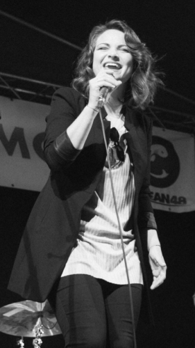 Speváčka z kapely KOLOREZ band emotívne spieva do mikrofónu počas živého vystúpenia na pódiu.