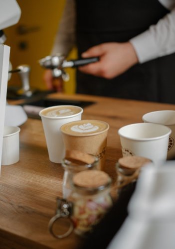 Čerstvo pripravené cappuccino s latte art v papierových pohároch na drevenom pulte mobilného kávového baru.