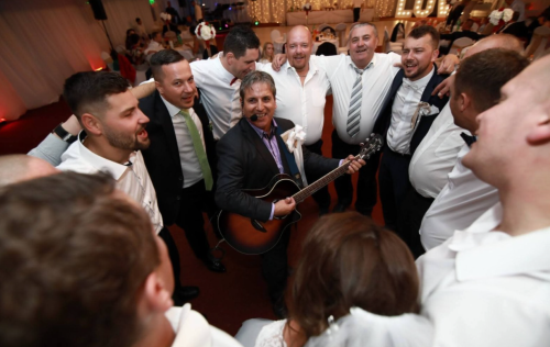Starejší s gitarou v obklopení spievajúcich svadobčanov počas svadobnej zábavy