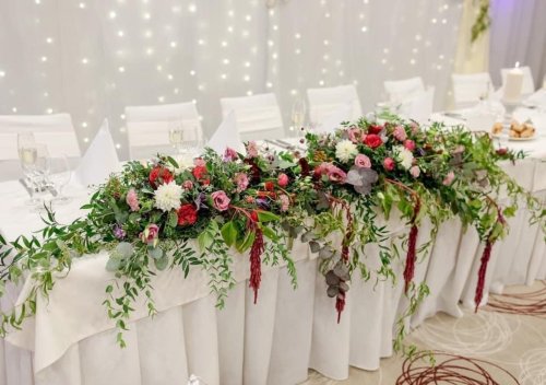 Elegantná kvetinová výzdoba na hlavnom svadobnom stole v rámci aranžérskych a floristických služieb s bielym pozadím a svetielkami.