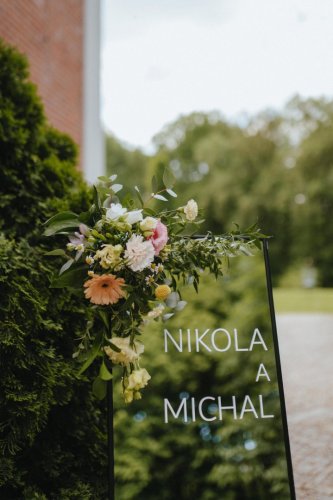 Elegantná svadobná uvítacia tabuľa z čierneho skla s menami Nikola a Michal, zdobená kvetinovým aranžmánom od LU.C design.
