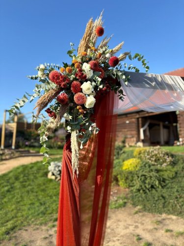 Detailný pohľad na kvetinovú dekoráciu svadobného oblúka od Haha Decoration s červenými a bielymi kvetmi a pampovou trávou.