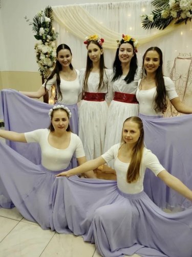 Skupinová fotografia súboru Svadobné čepčenie Ružičky v bielych a fialových kostýmoch pred slávnostným pozadím.