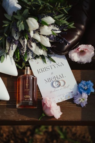 Svadobné detaily od Kristýna Revaj | By Bride zachytávajúce oznámenie, obrúčky, kyticu a parfum na drevenom podklade.