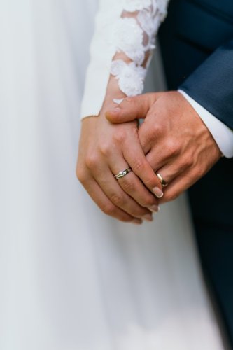 Detailný záber na prepletené ruky nevesty a ženícha so svadobnými obrúčkami, zachytený fotografkou Lenkou Holčíkovou.