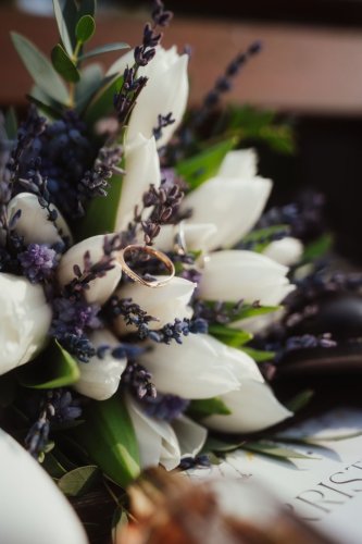 Detailný záber na svadobné obrúčky položené na kytici z bielych tulipánov a levandule od Kristýna Revaj | By Bride