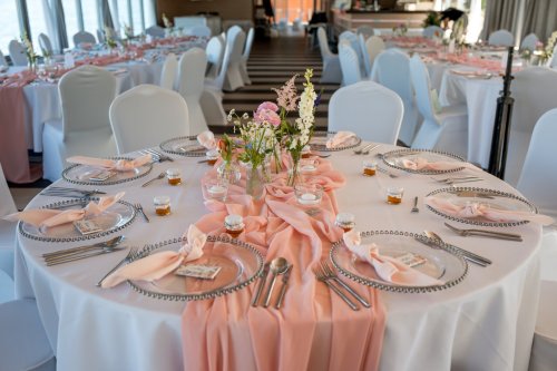 Elegantne prestretý okrúhly svadobný stôl s jemným ružovým behúňom, kvetinovou výzdobou a darčekmi pre hostí od ESTERI.