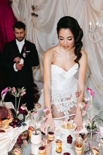 Elegantná nevesta v bielych šatách aranžuje exkluzívny svadobný catering od Empresa catering & events, zatiaľ čo ženích stojí v pozadí.
