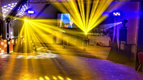 Profesionálne svetelné efekty a technika od DJ-a a moderátora na svadobnom parkete so žltými lúčmi.