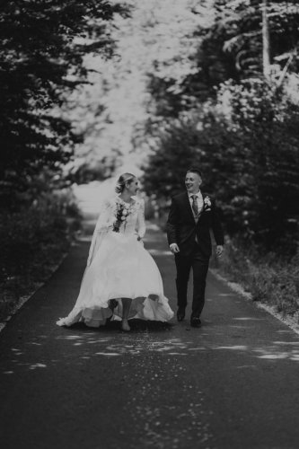 Čiernobiela fotografia od Lenky Holčíkovej zachytávajúca smejúci sa mladomanželský pár kráčajúci po lesnej ceste.
