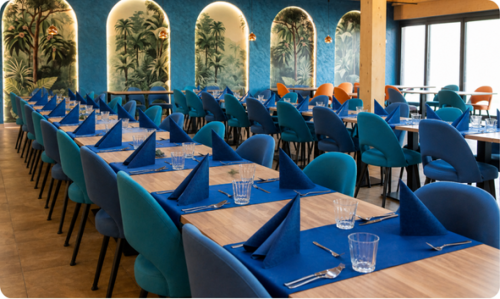 Interiér reštaurácie Restaurant AZURO s prestretými stolmi v modrej farbe a tropickými maľbami na stenách pripravený na svadobnú hostinu.