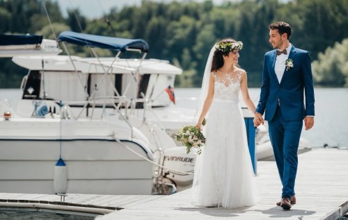 Novomanželia sa držia za ruky a prechádzajú sa po móle v Rezorte MARINA LIPTOV pri zaparkovaných lodiach.