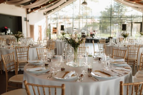 Elegantne prestreté okrúhle stoly so zlatými stoličkami v presvetlenom interiéri event house Humno Demänová.