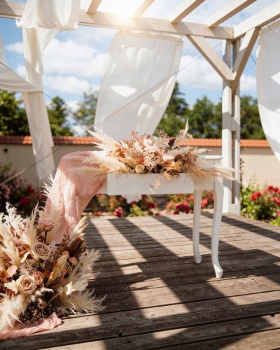 Elegantne zdobený biely svadobný stôl s kvetinovou výzdobou v boho štýle pod altánkom v areáli Tvrz KRASSA.